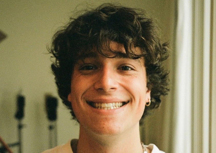 A man with curly brown hair and a gold hoop earringx